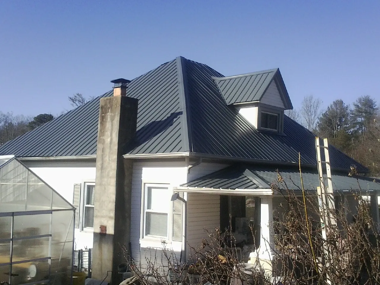 Dark blue standing seam metal roof on a white farmhouse with dormer — Slate & Tile Roof Repair by Roofing Brothers in Harlan