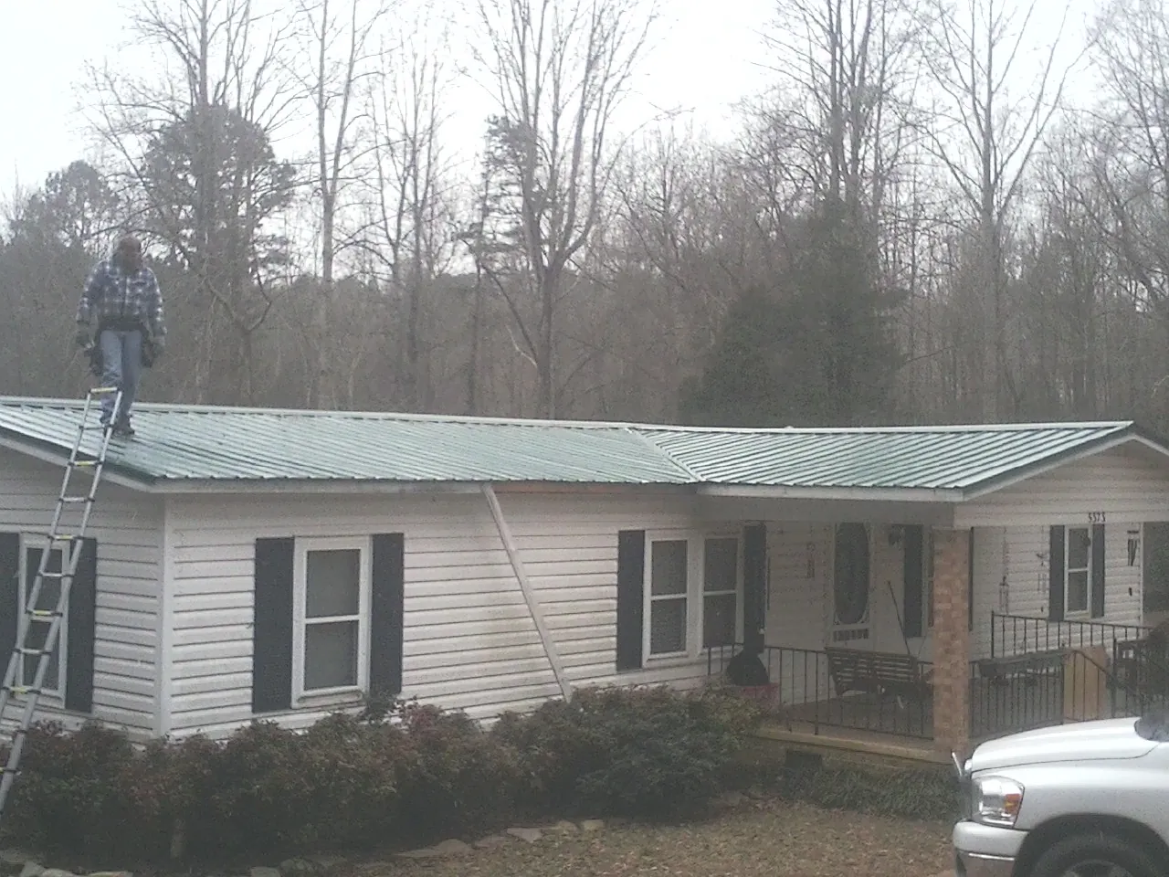 Worker on a ladder beside a new green metal roof on a ranch home in Harlan