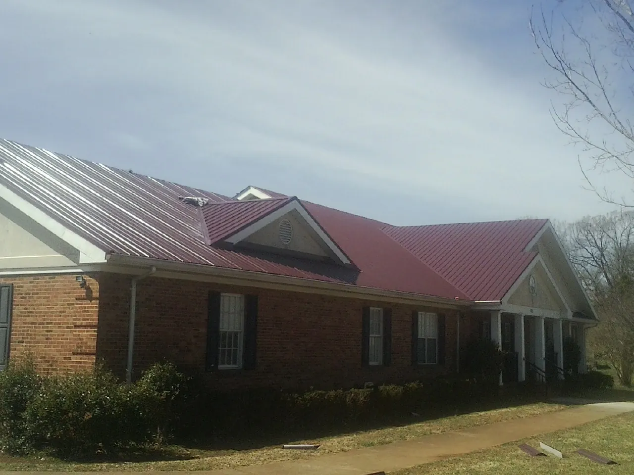 Red metal roof with gabled entries on a long brick building, from a Hail Damage Roof Repair job in Harlan