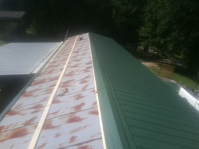 Old rusted panels beside newly installed green metal roofing — Wind Damage Roof Repair by Roofing Brothers in Harlan