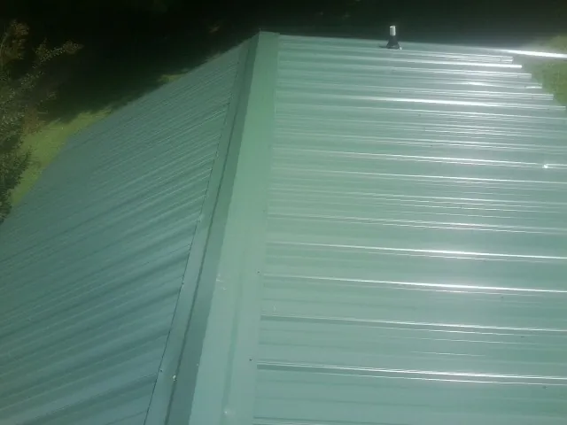 New green metal panels meeting at the ridge of a roof — Flat Roof Repair work by our crew in Harlan