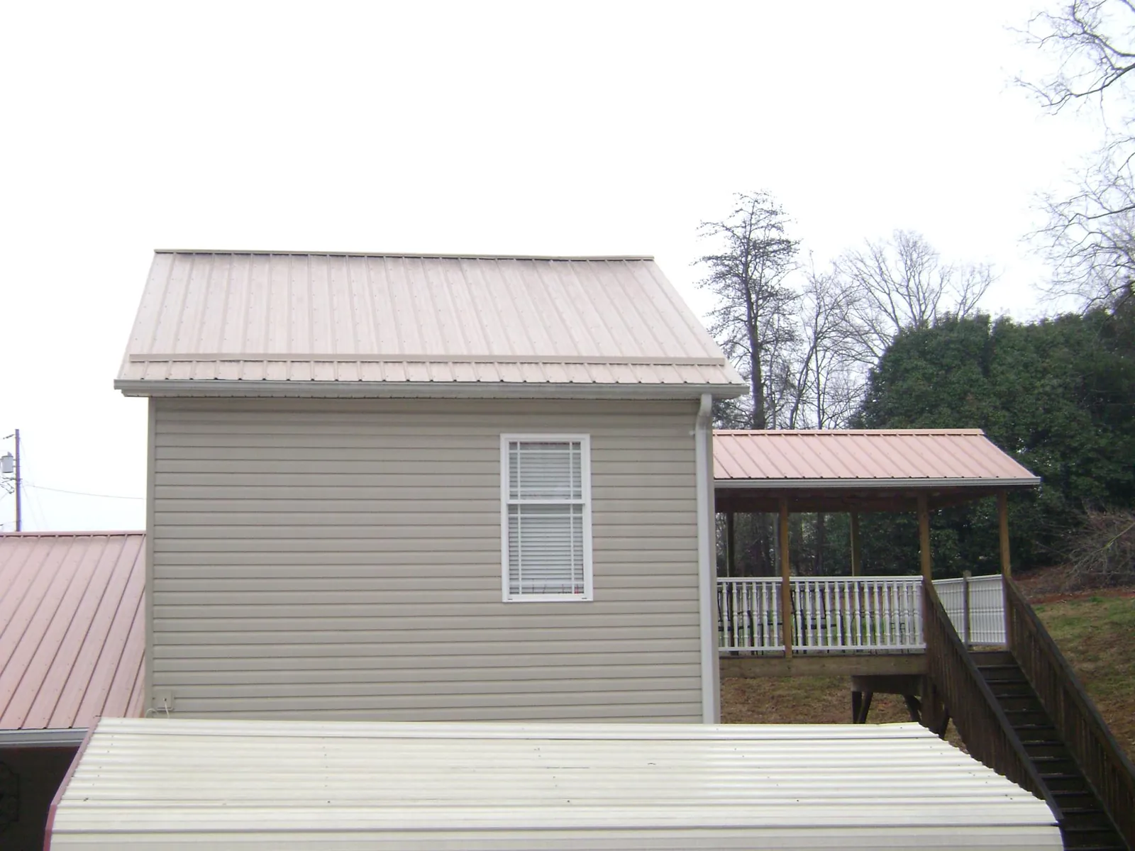 Tan metal roofs on a two story addition and attached porch, from a Roof Replacement job in Harlan